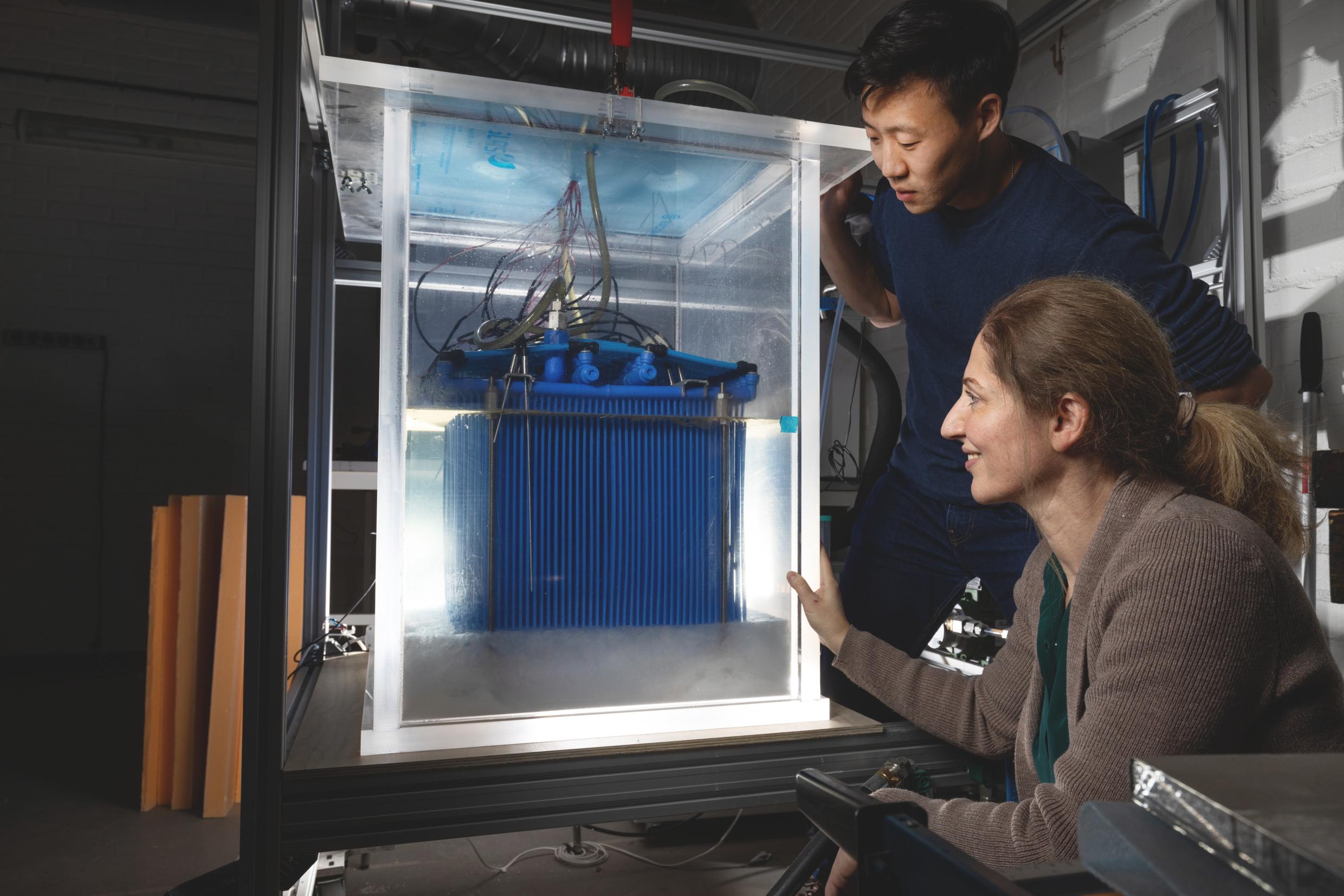 A man and a woman look inside a glass case filled with wires and blue metal container.