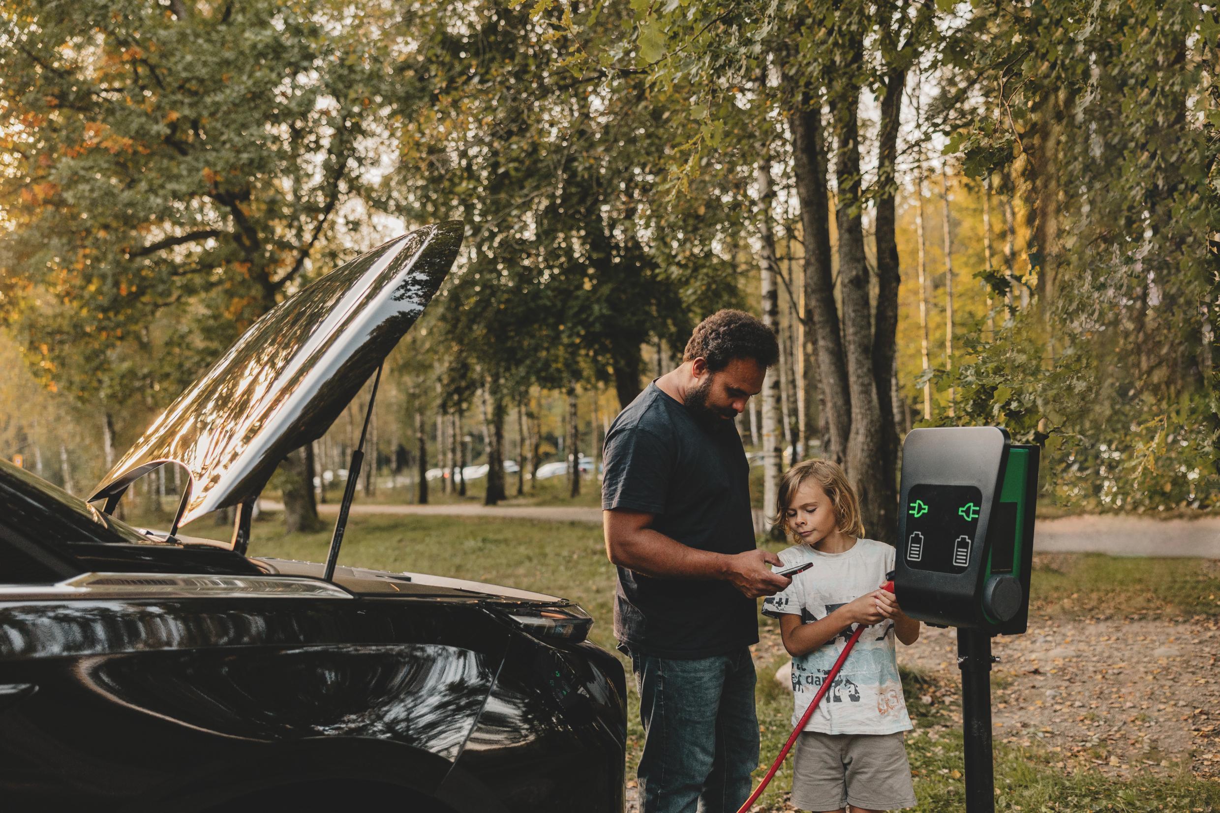 A man and a boy standing by a charging station in nature.