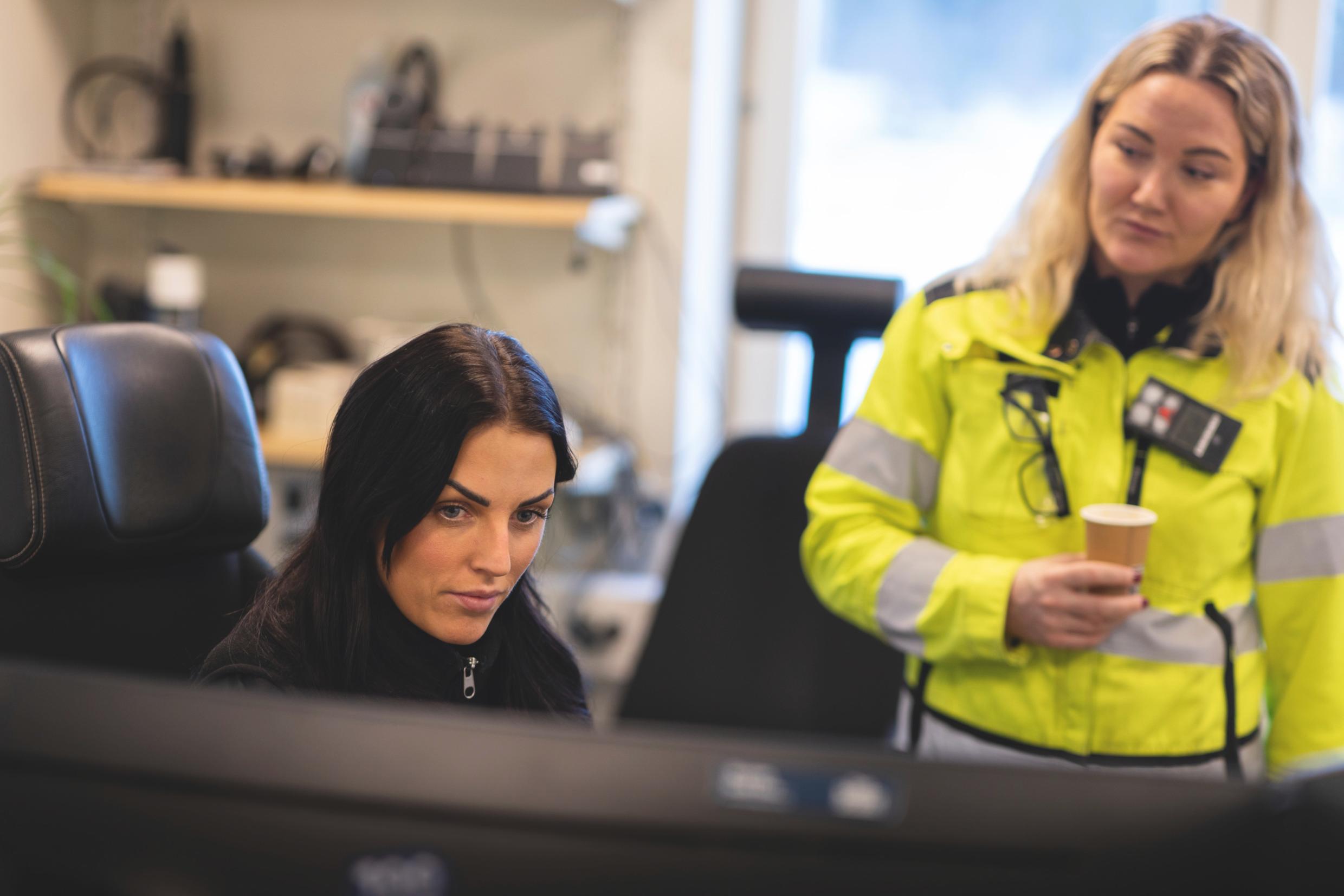 Two women in an office, one of them wearing a high-visibility vest.