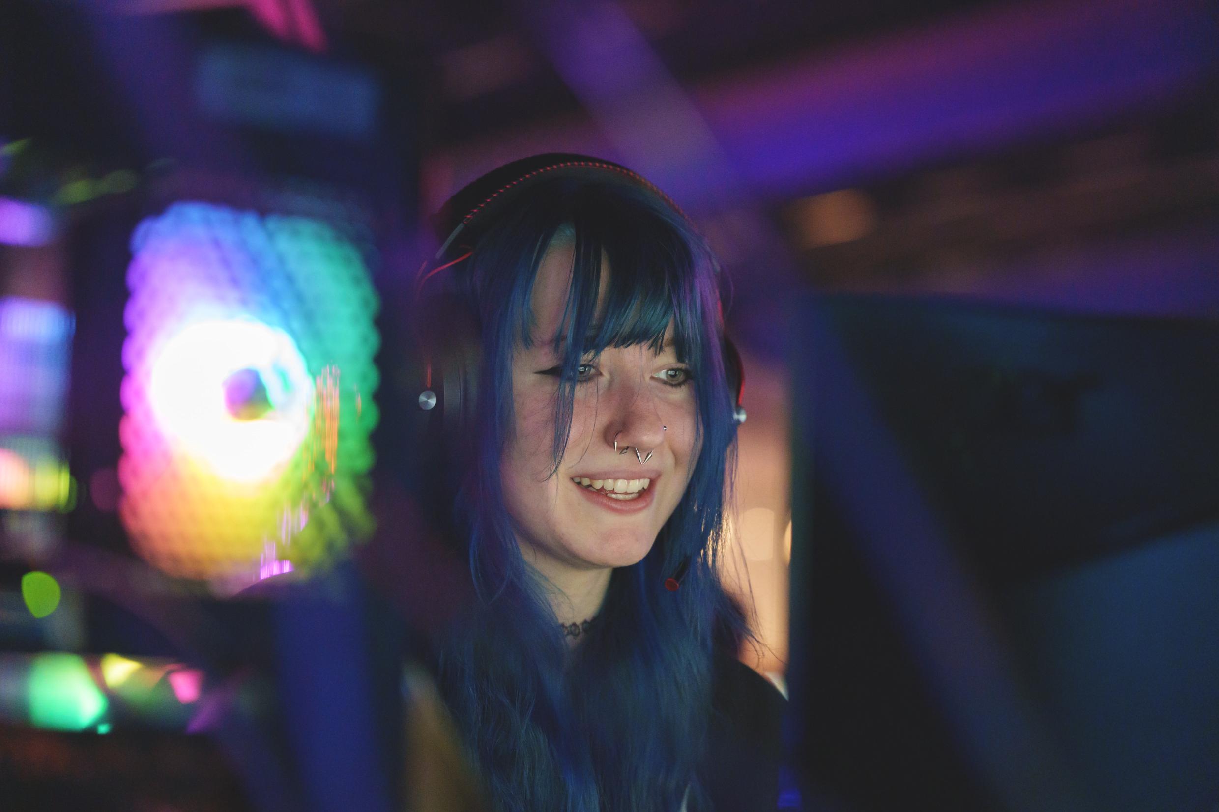 A girl with blue hair sitting in front of a computer screen.