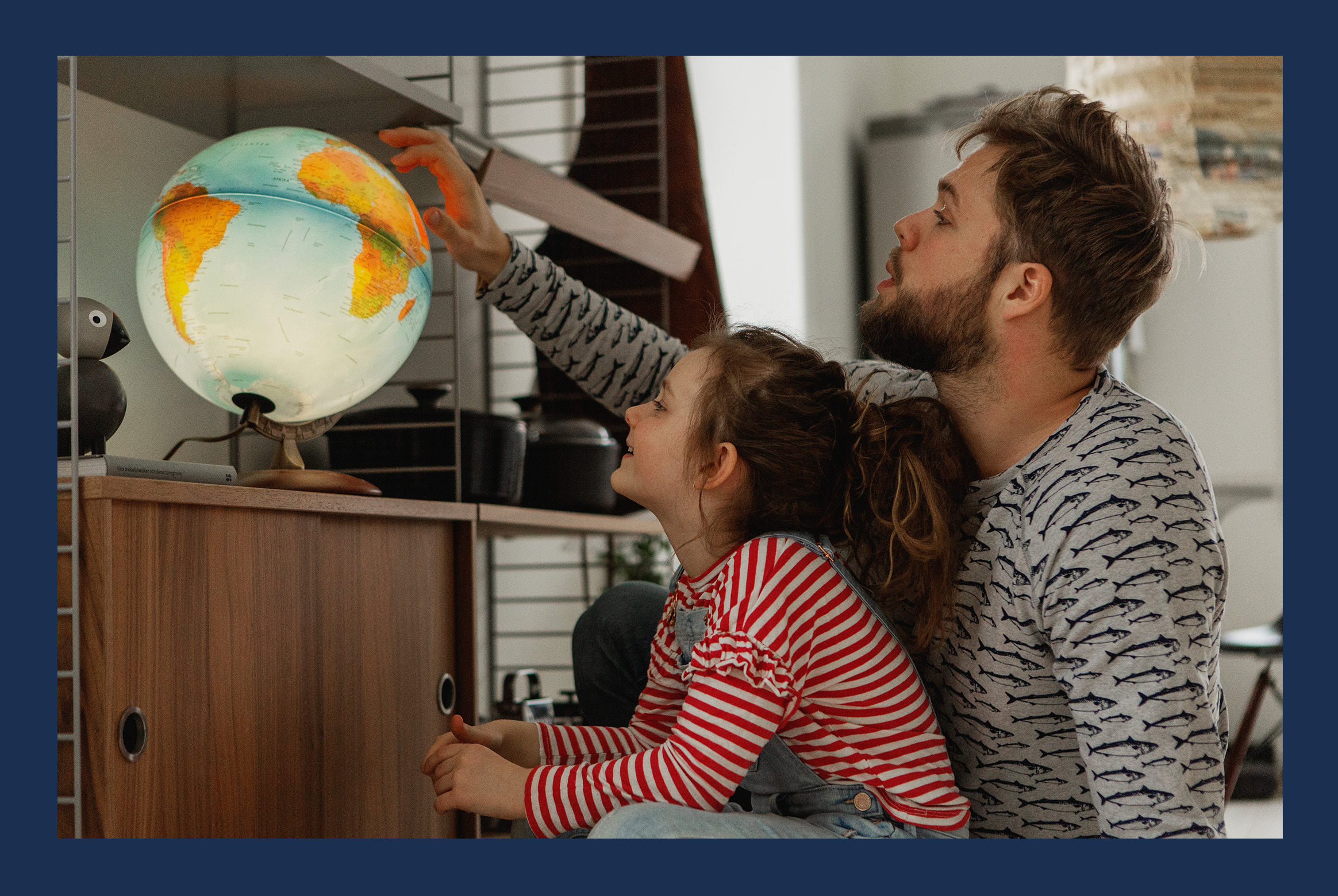 A child and her father looking at a globe lamp.