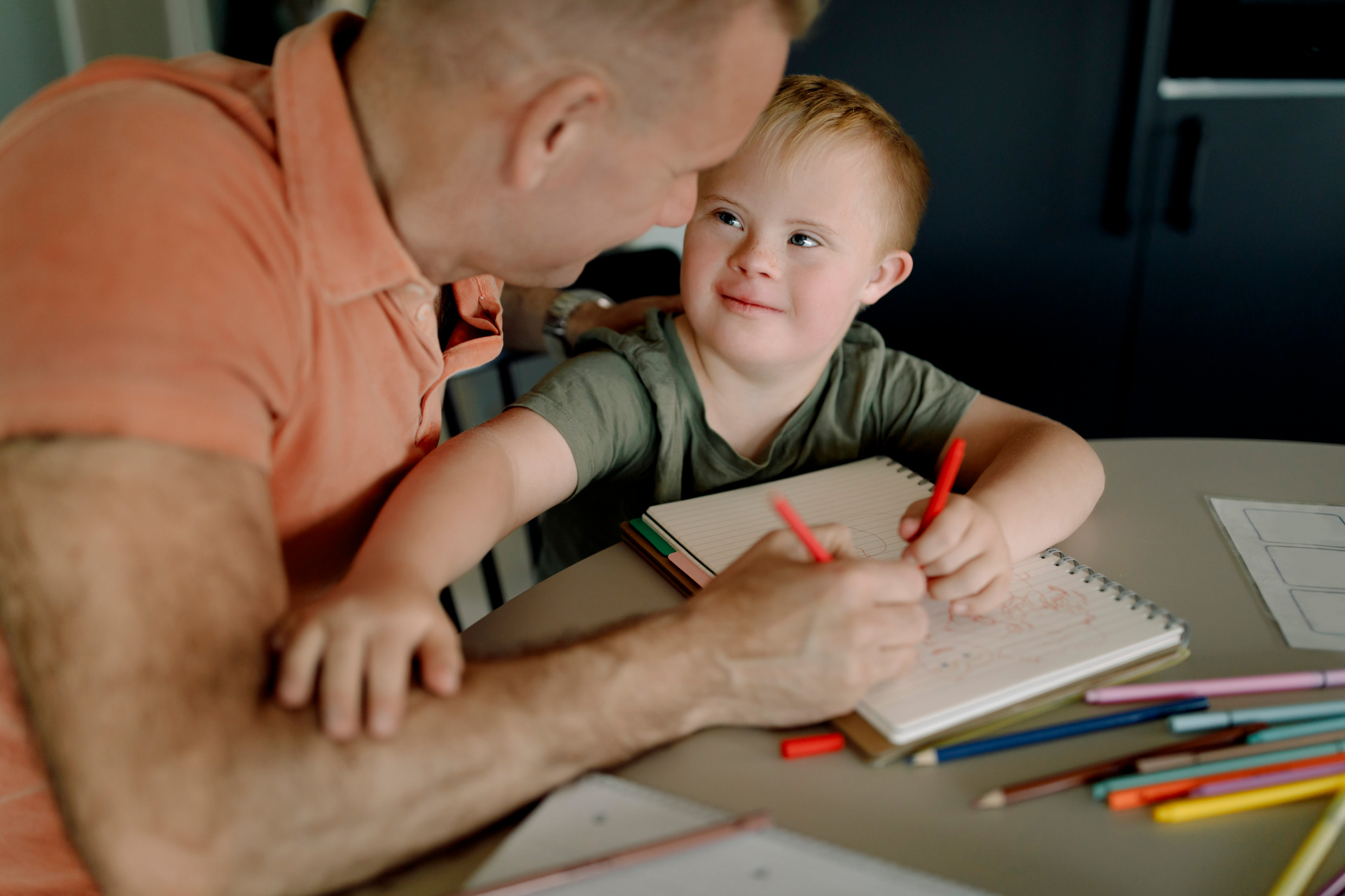 A father and young child making a drawing together.
